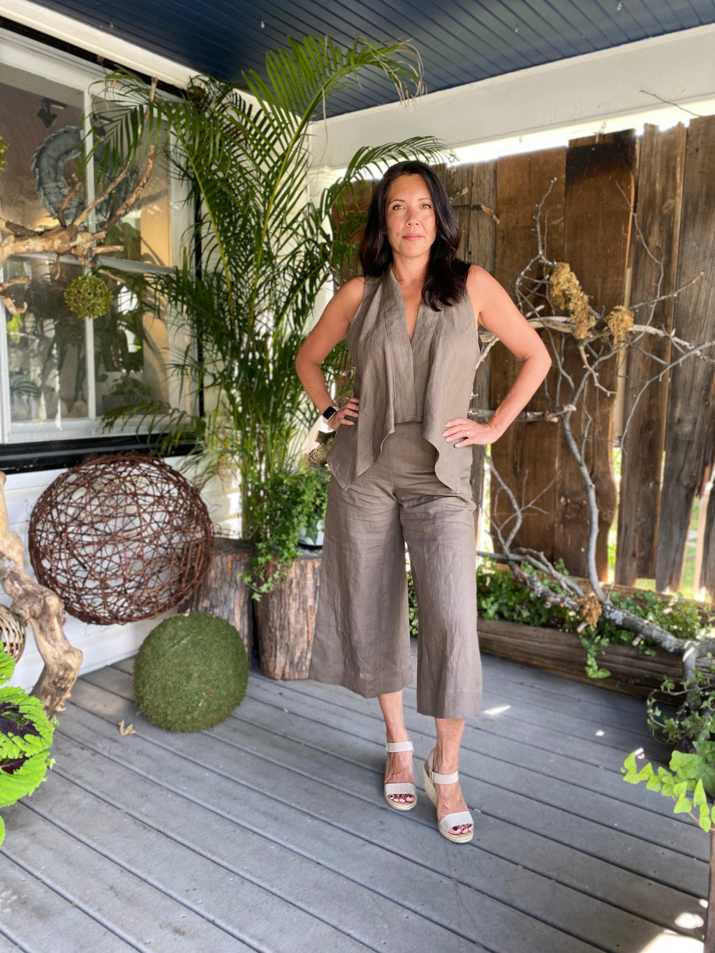 Cropped wide leg taupe linen  pants paired with matching taupe linen flowy Bonnie vest. Model stands on deck of Manotick Mill Street Florist. She is 5'10" tall and wears size M