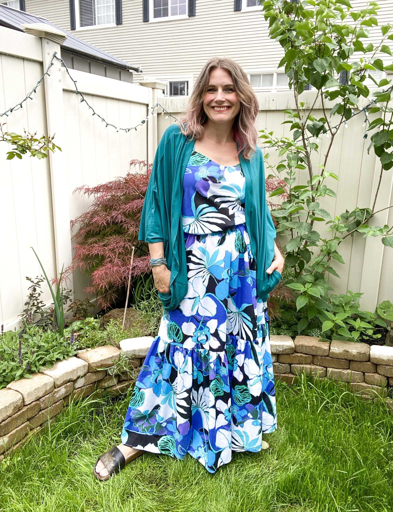 Stephanie wears the Carlile dress in blue floral cotton with a peacock jersey Pippa shrug over top. She wears a S/M