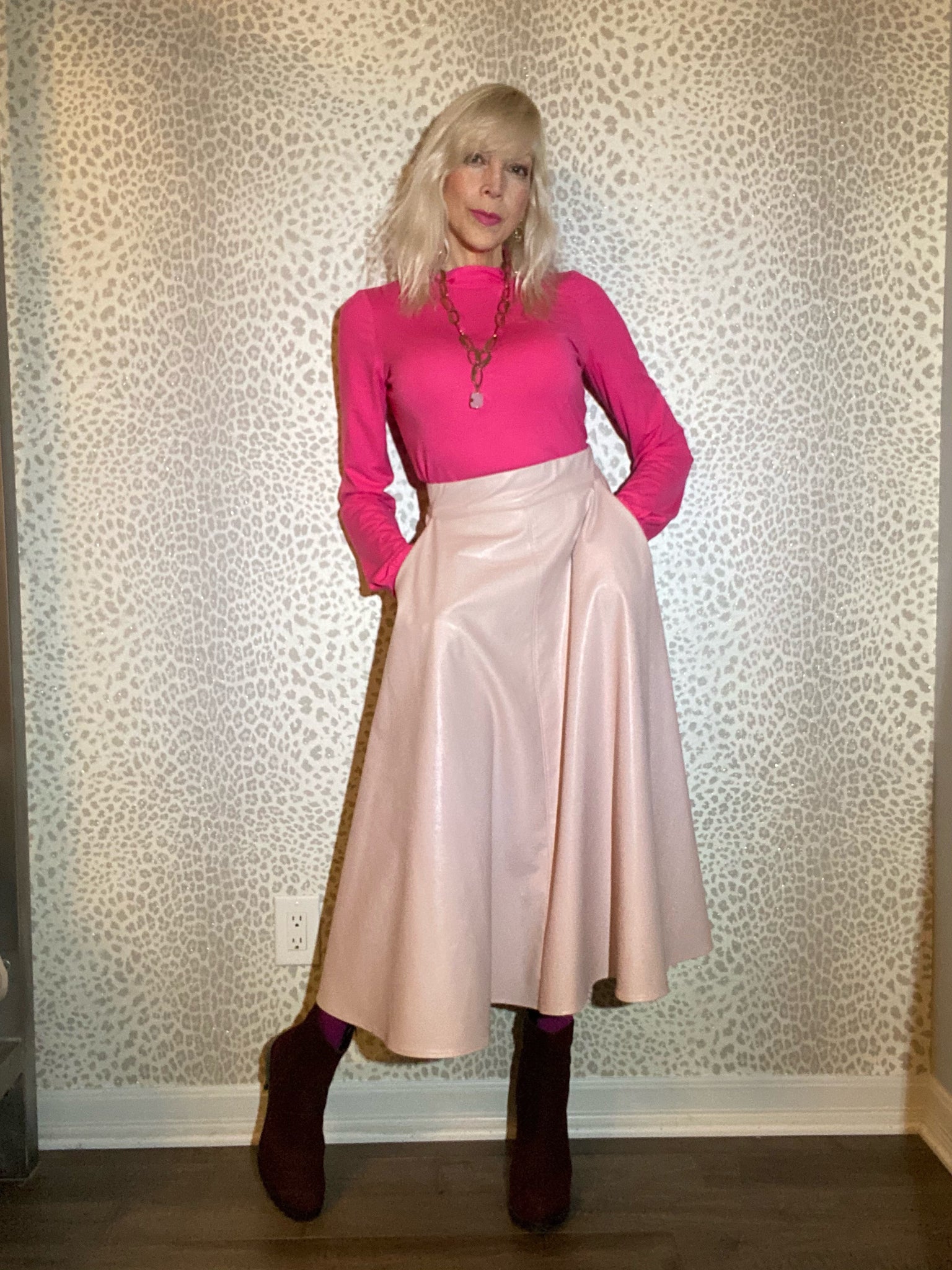 Judy wears a pink turtleneck with short 60s-inspired collar and gathered modified bishop sleeves. She paired it with a blush pink leatherette Oma Vera circle skirt, fuschia tights and dark red suede boots