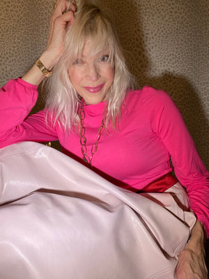 Judy wears a pink turtleneck with short 60s-inspired collar and gathered modified bishop sleeves. She paired it with a blush pink leatherette Oma Vera circle skirt, fuschia tights and dark red suede boots. She sits with legs up and head resting against her hand